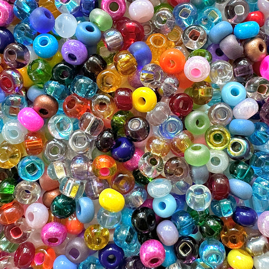 A close-up image of a colorful assortment of Confetti 6/0 Czech Seed Bead Mix in various shapes and translucent colors including blue, pink, green, yellow, and purple.