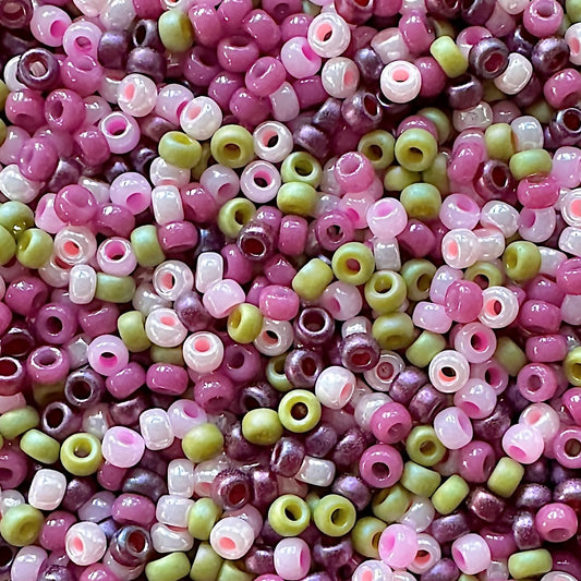 A close-up view of a collection of small, multicolored Cherry Blossom 11/0 Miyuki seed beads in shades of pink, purple, and green, showcasing their glossy surfaces and various shapes.