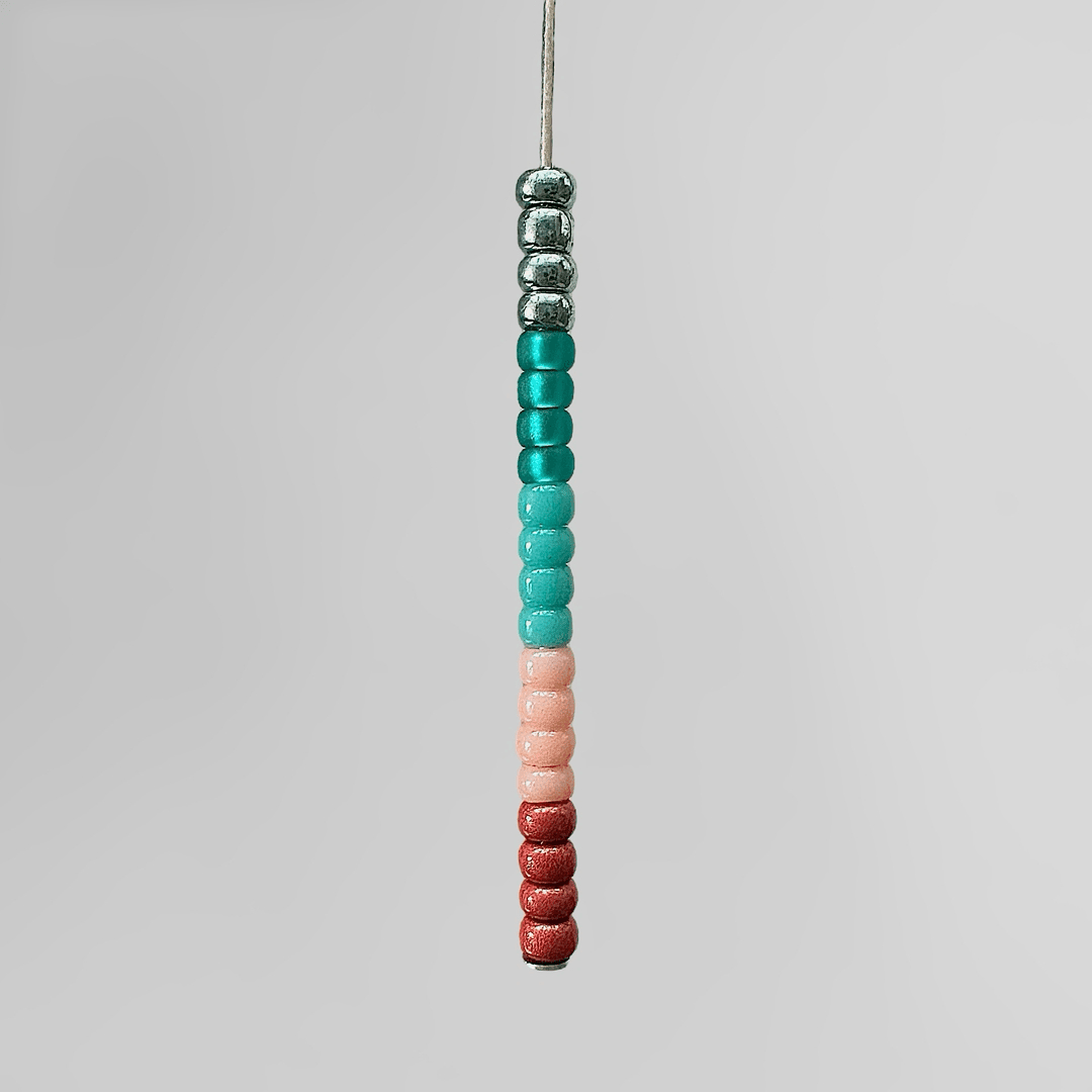 Red, peach, and teal Miyuki seed beads strung on a wire.