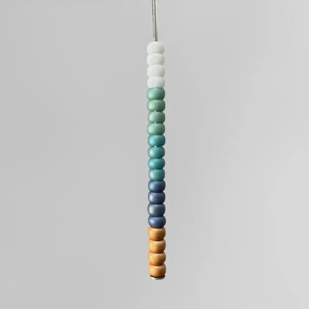 Matte gold, blue, turquoise, teal, and white Miyuki seed beads strung on a wire.