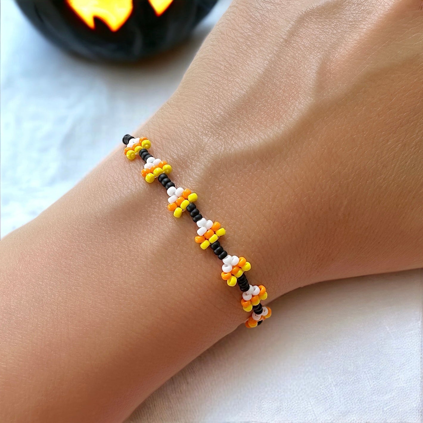 Beaded candy corn chain bracelet on a woman's wrist with a white cloth in the background