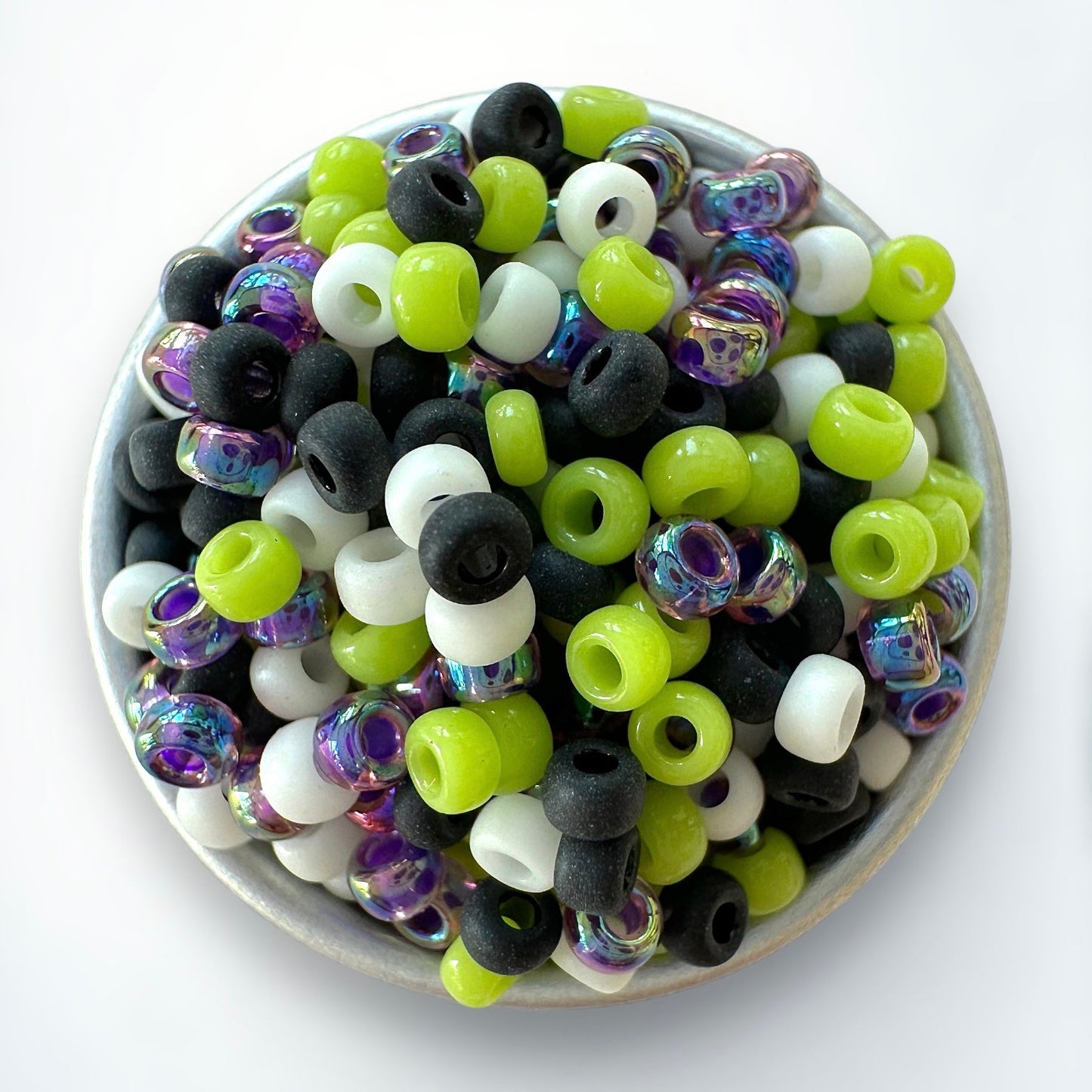 Mix of purple, black, white, and green Miyuki 11/0 seed beads by The Bead Mix in a silver container with a white background