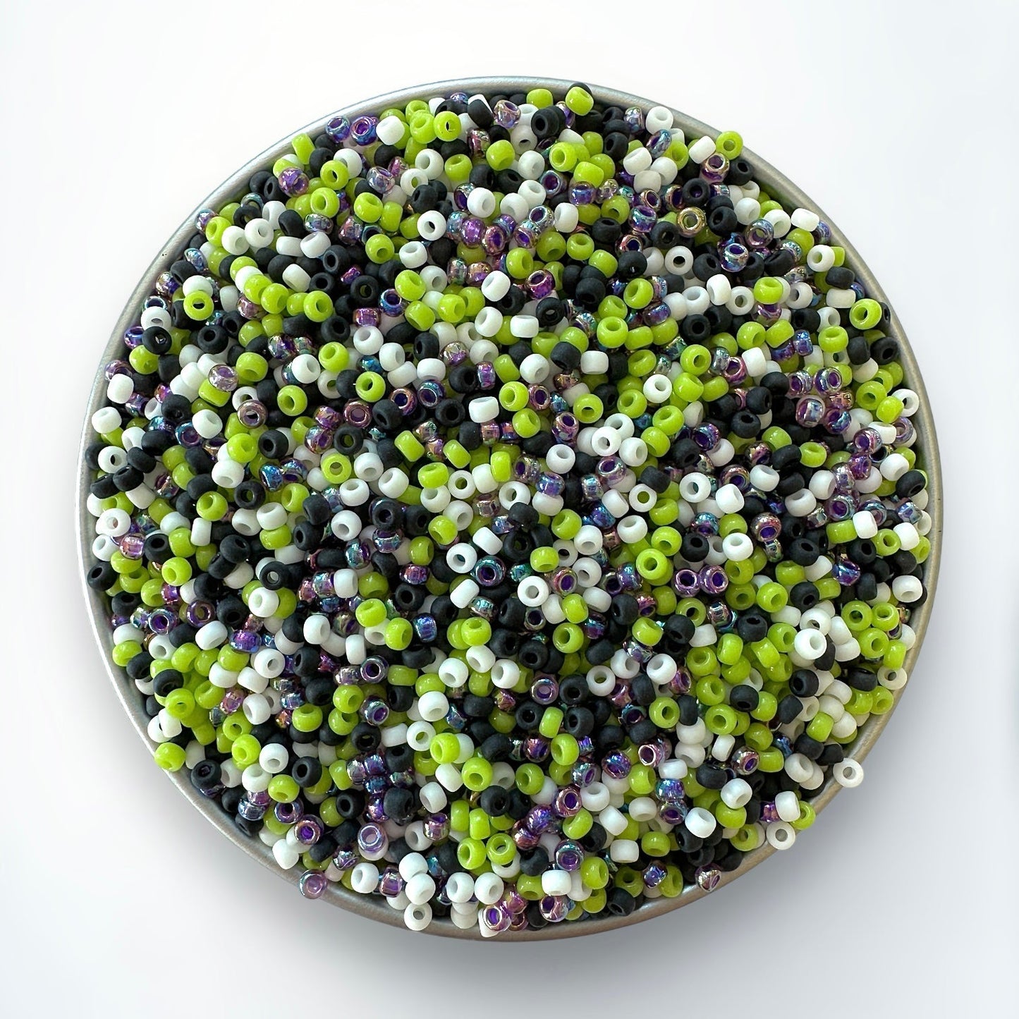 Mix of purple, black, white, and green Miyuki 11/0 seed beads by The Bead Mix in a silver container with a white background
