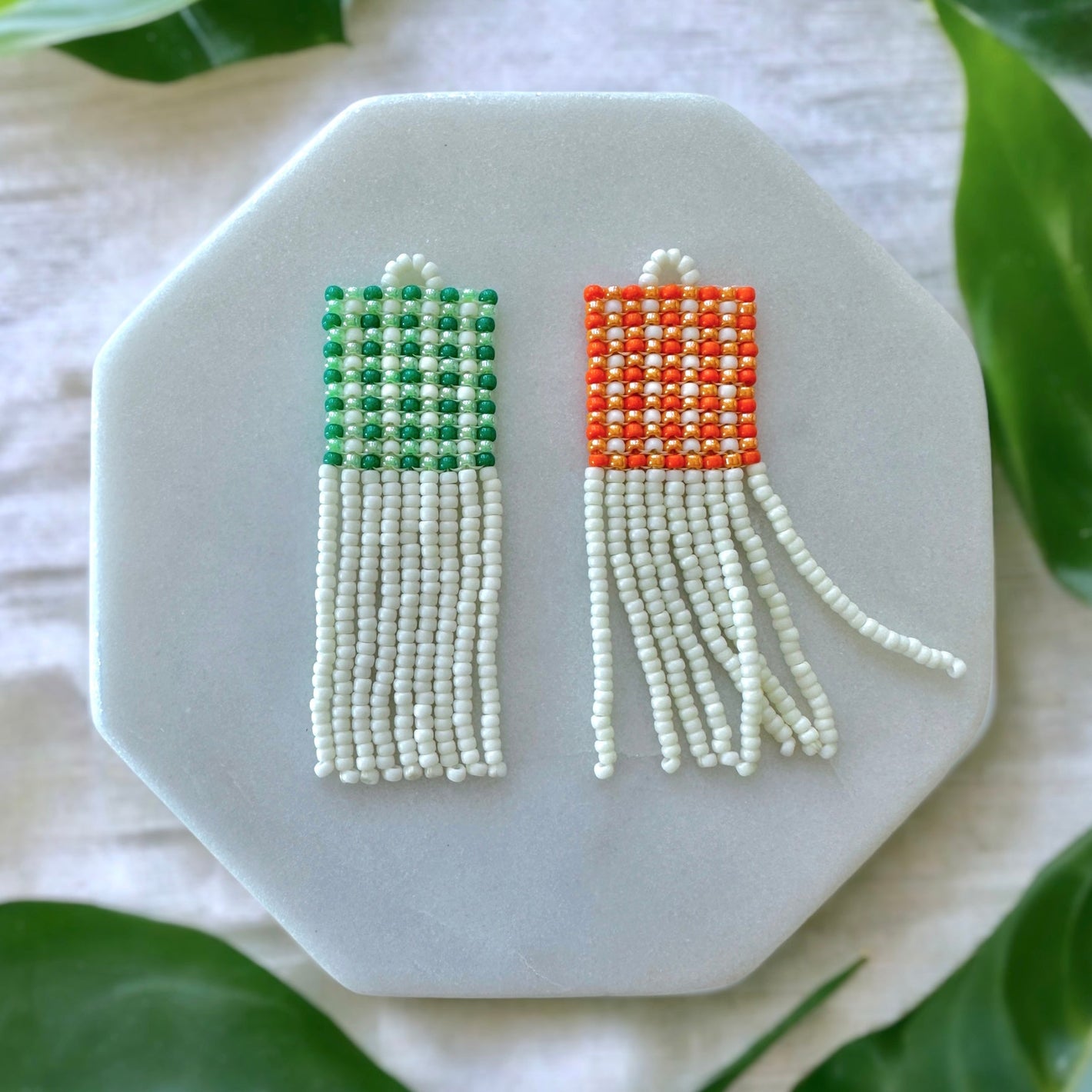 Set of two beaded fringe earrings with a green and orange gingham pattern on white marble coaster on a white cloth background