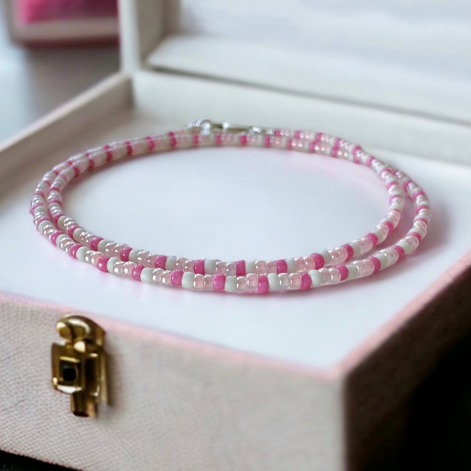 A dainty seed bead necklace made with pink and cream 11/0 Miyuki seed beads placed neatly in a pink jewelry box