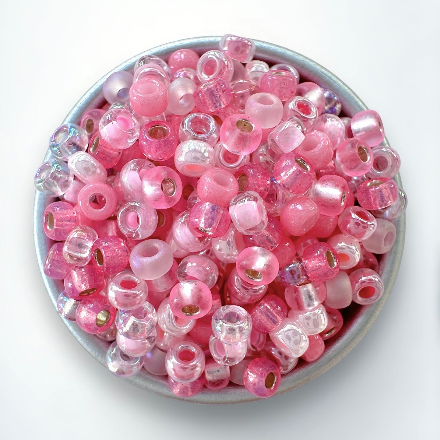 Mix of pink miyuki 11/0 seed beads by The Bead Mix in a silver container with a white background