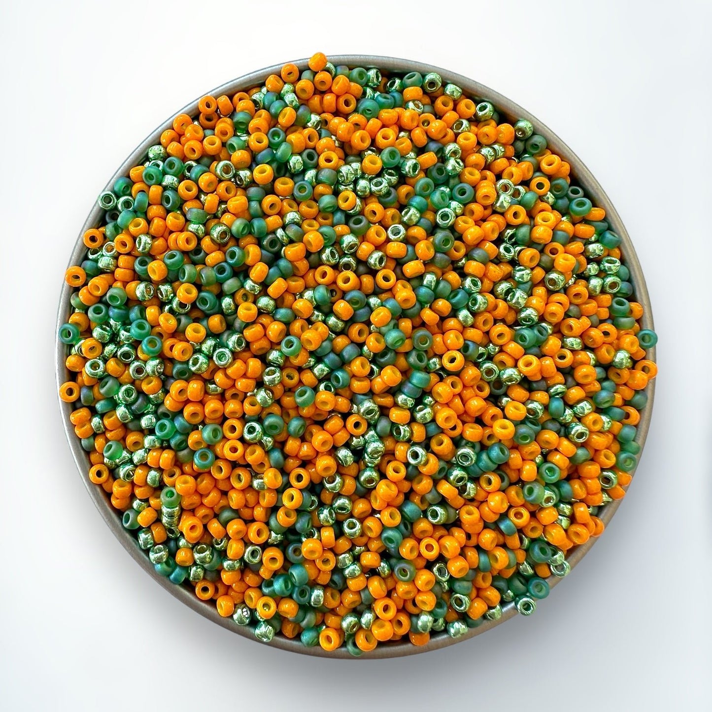 A mix of orange and green Miyuki 11/0 seed beads mixes created by The Bead Mix in a silver container with a white background