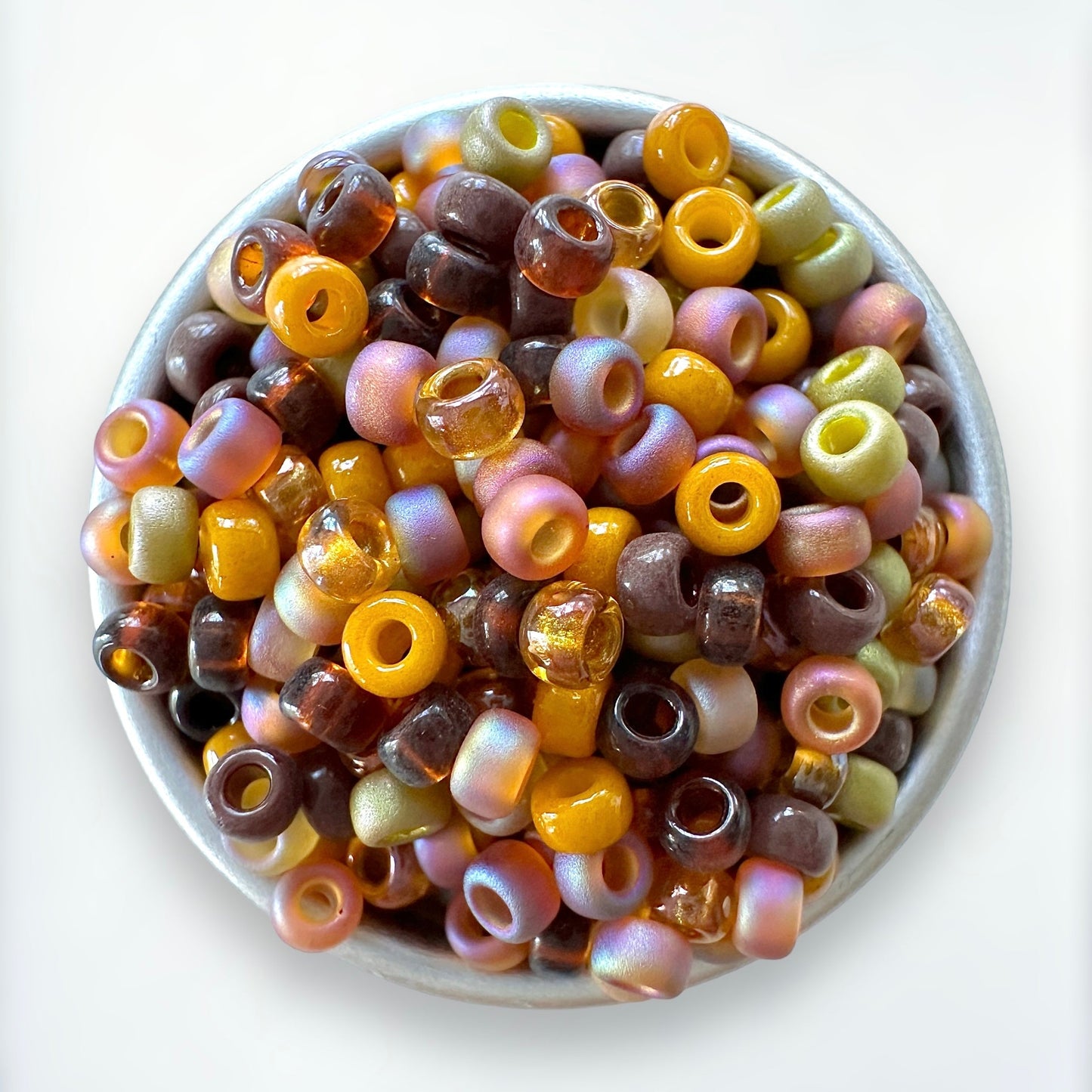 Close-up of Miyuki round seed beads in autumn colors in a small metal container with a white background.