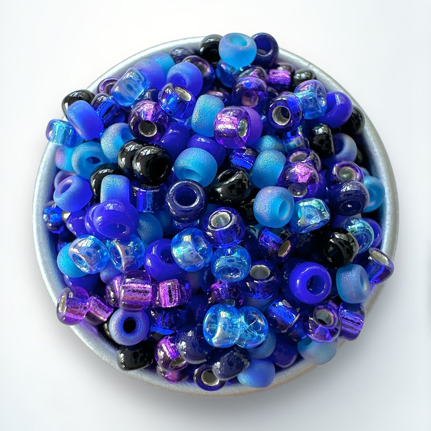 A mix of blue and purple Miyuki 11/0 seed beads created by The Bead Mix in a silver container with a white background