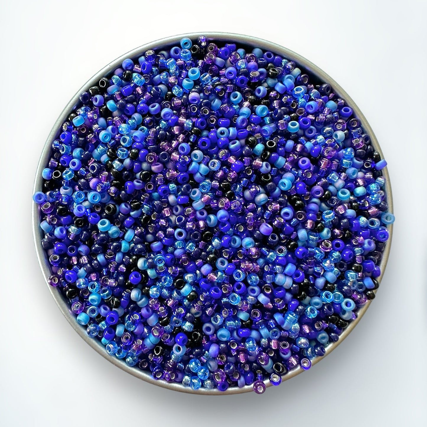 A mix of blue and purple Miyuki 11/0 seed beads created by The Bead Mix in a silver container with a white background