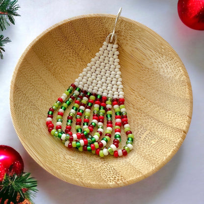 A beaded brick stitch earring with swoop fringe made with cream and christmas colored Miyuki 11/0 seed beads in a wooden dish on a white background surrounded by Christmas decorations