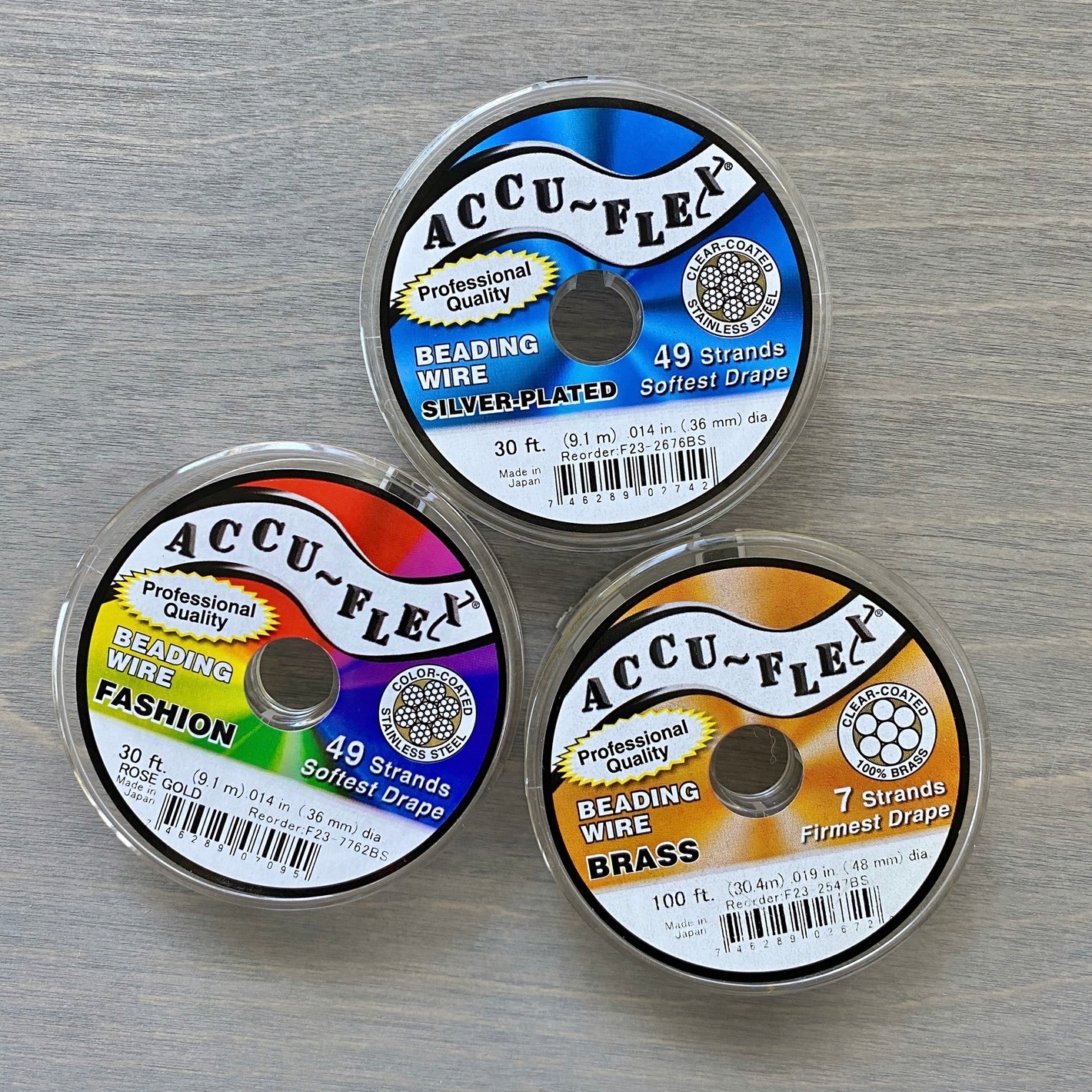 Three spools of Accu-Flex beading wire arranged on a gray textured surface.