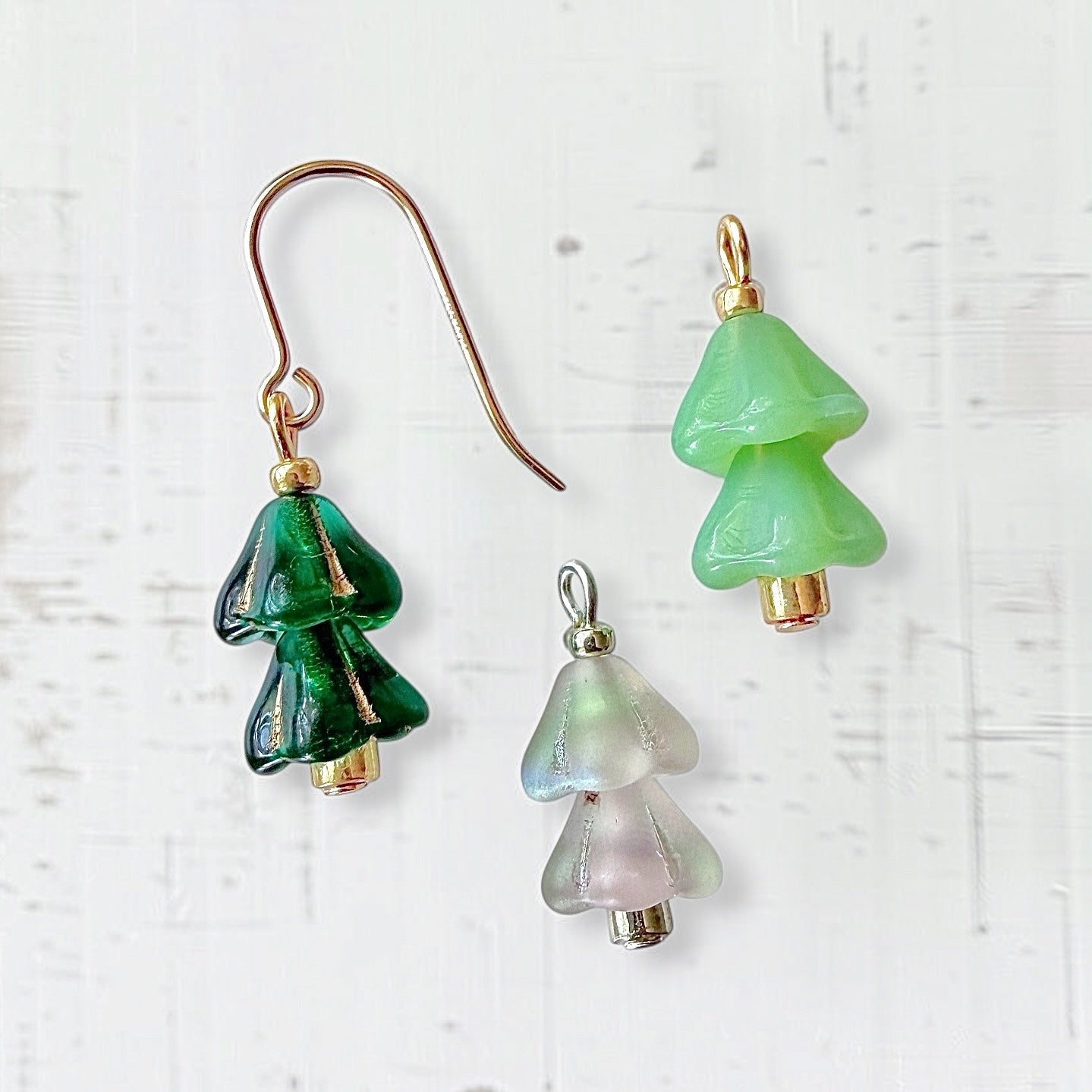 Glass beaded Christmas tree earrings and charms on a white textured background.
