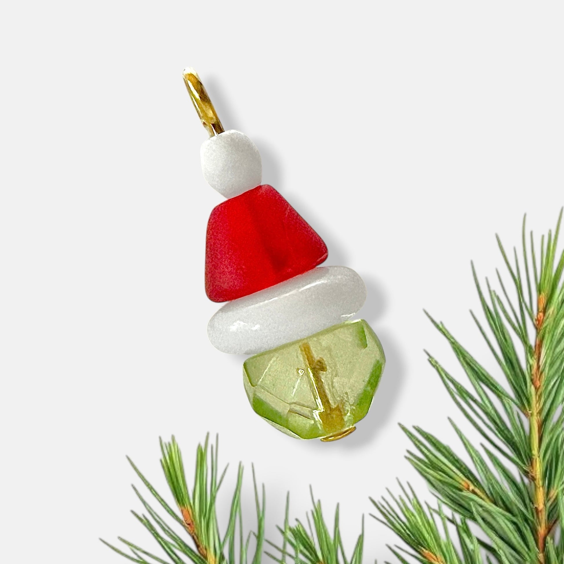 Beaded charm that resembles the grinch with a gold loop with a white background and pine needles.