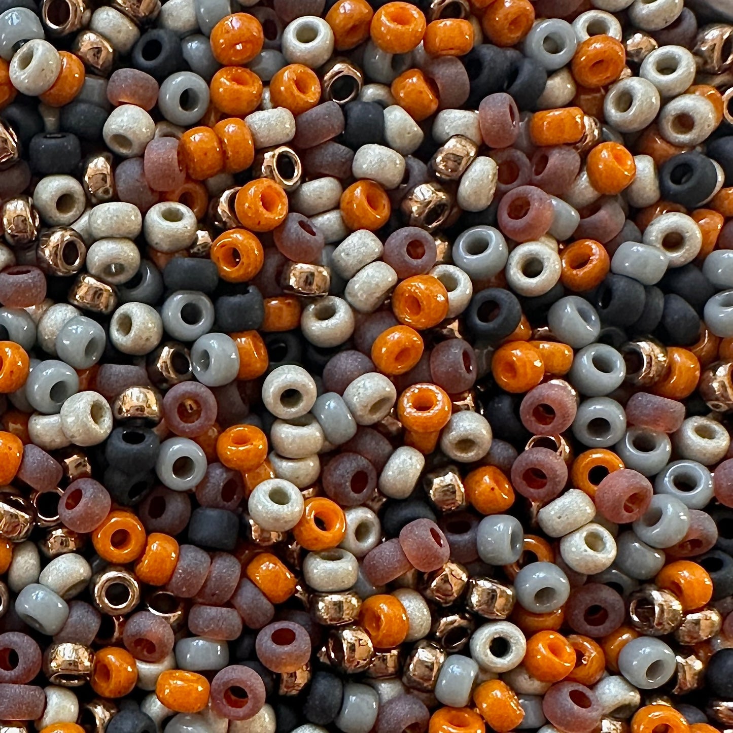 A mix of Miyuki round seed beads in shades or brown, black, orange, gray, and silver.