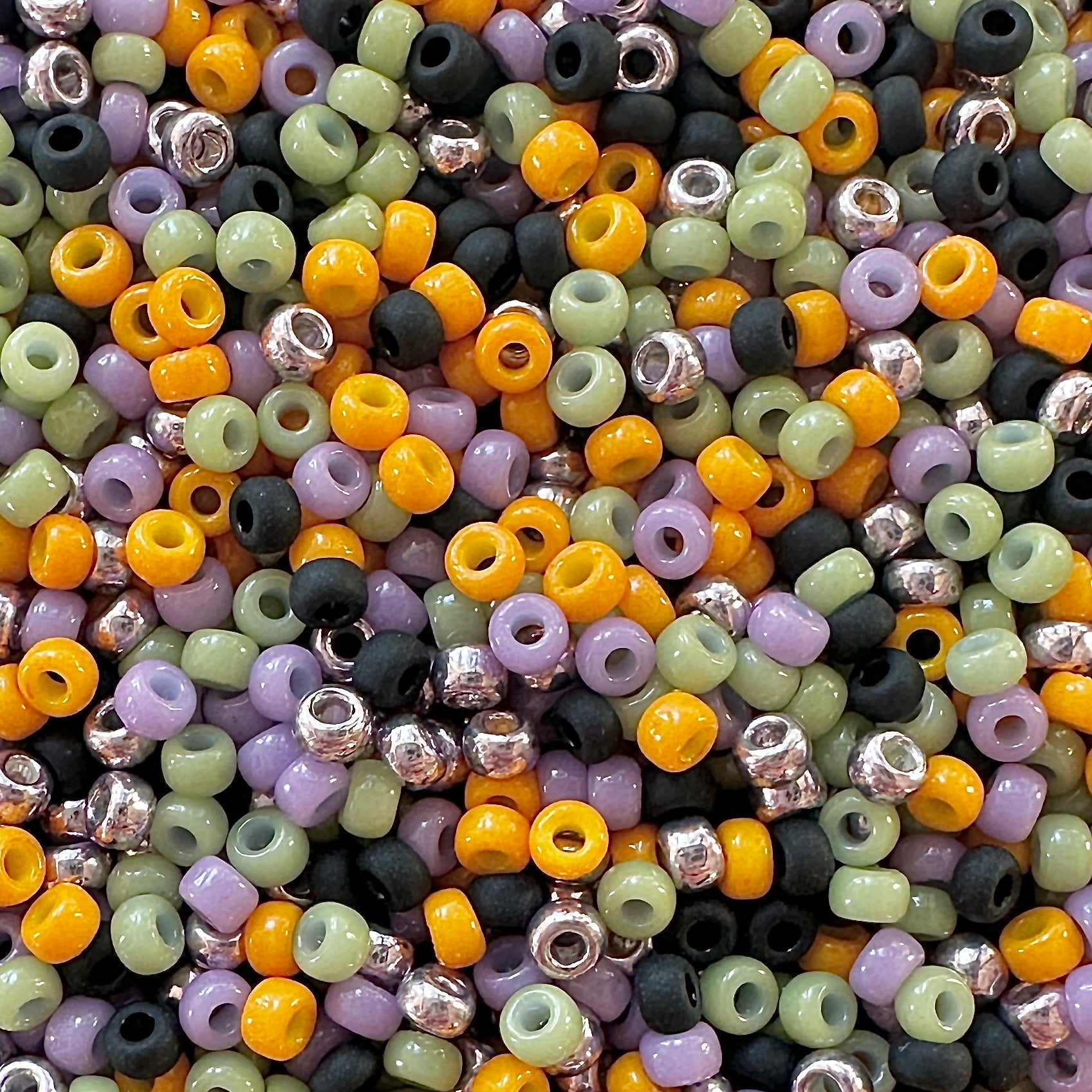Mix of Miyuki round seed beads in faded halloween colors including black, orange, green, and purple.