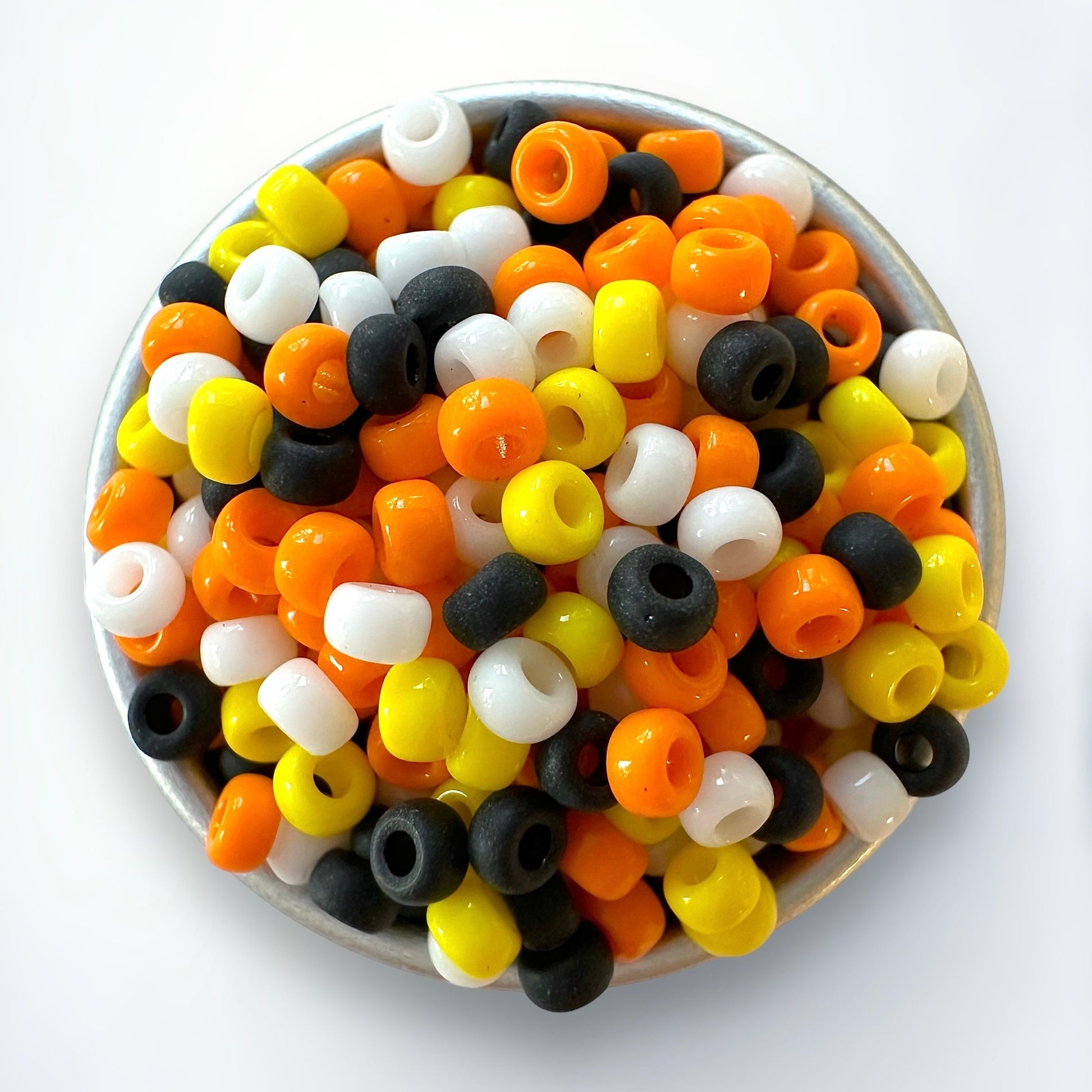 Mix of candy corn colored Miyuki 11/0 seed beads, including yellow, orange, white, and black in a silver container on a white background