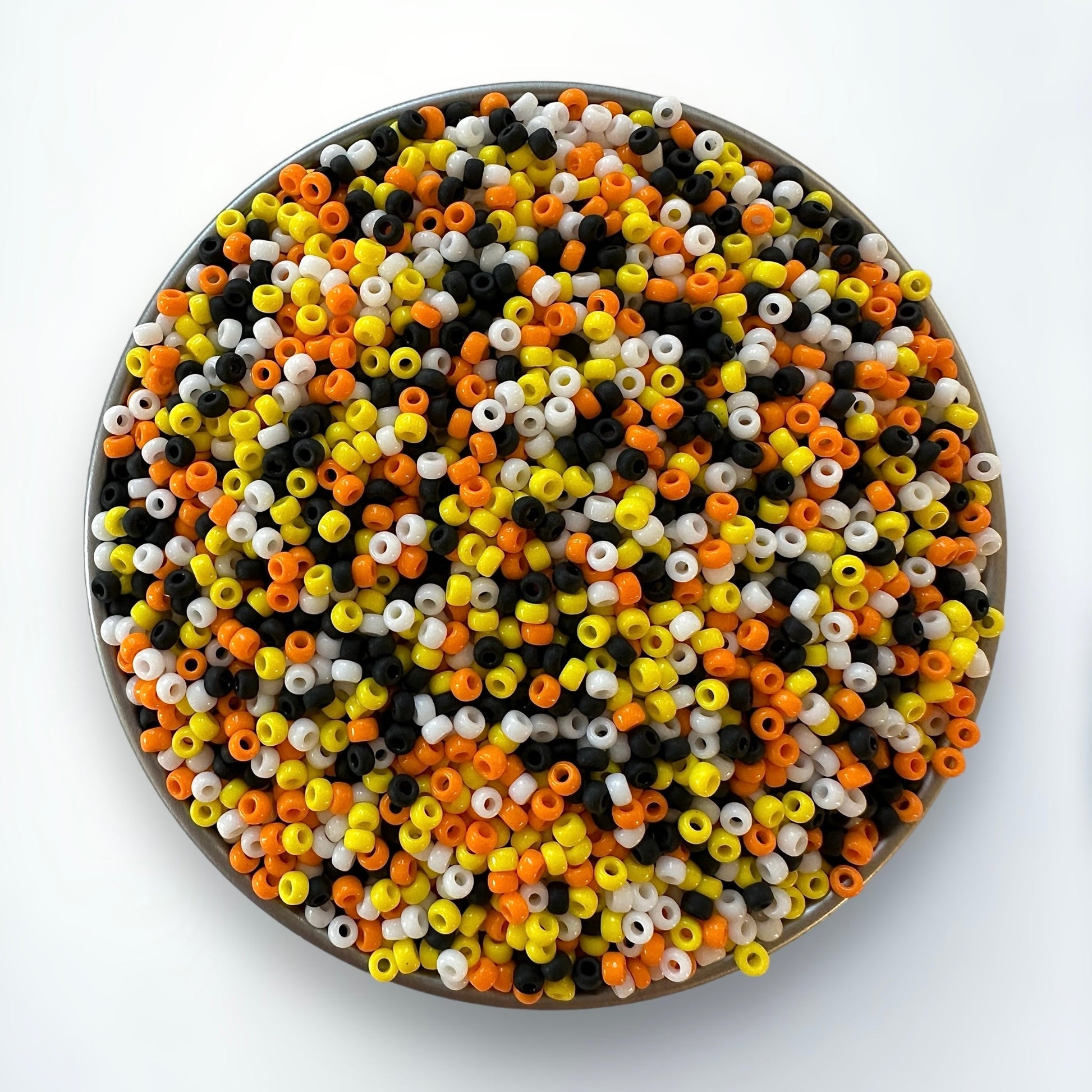 Mix of candy corn colored Miyuki 11/0 seed beads, including yellow, orange, white, and black in a silver container on a white background