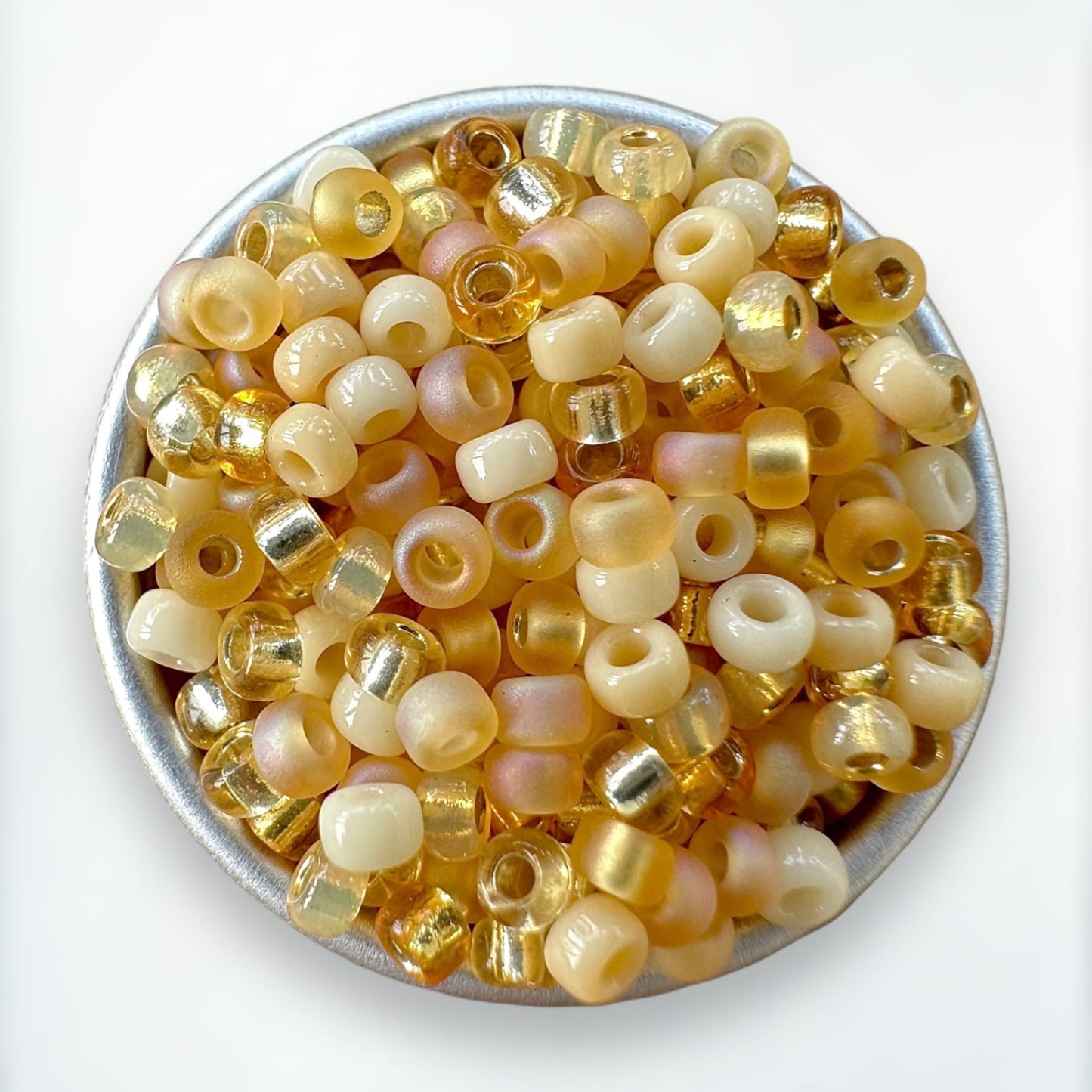 zoomed view of a mix of cream, topaz and gold Miyuki 11/0 seed beads created by The Bead Mix in a round silver tray with a white background