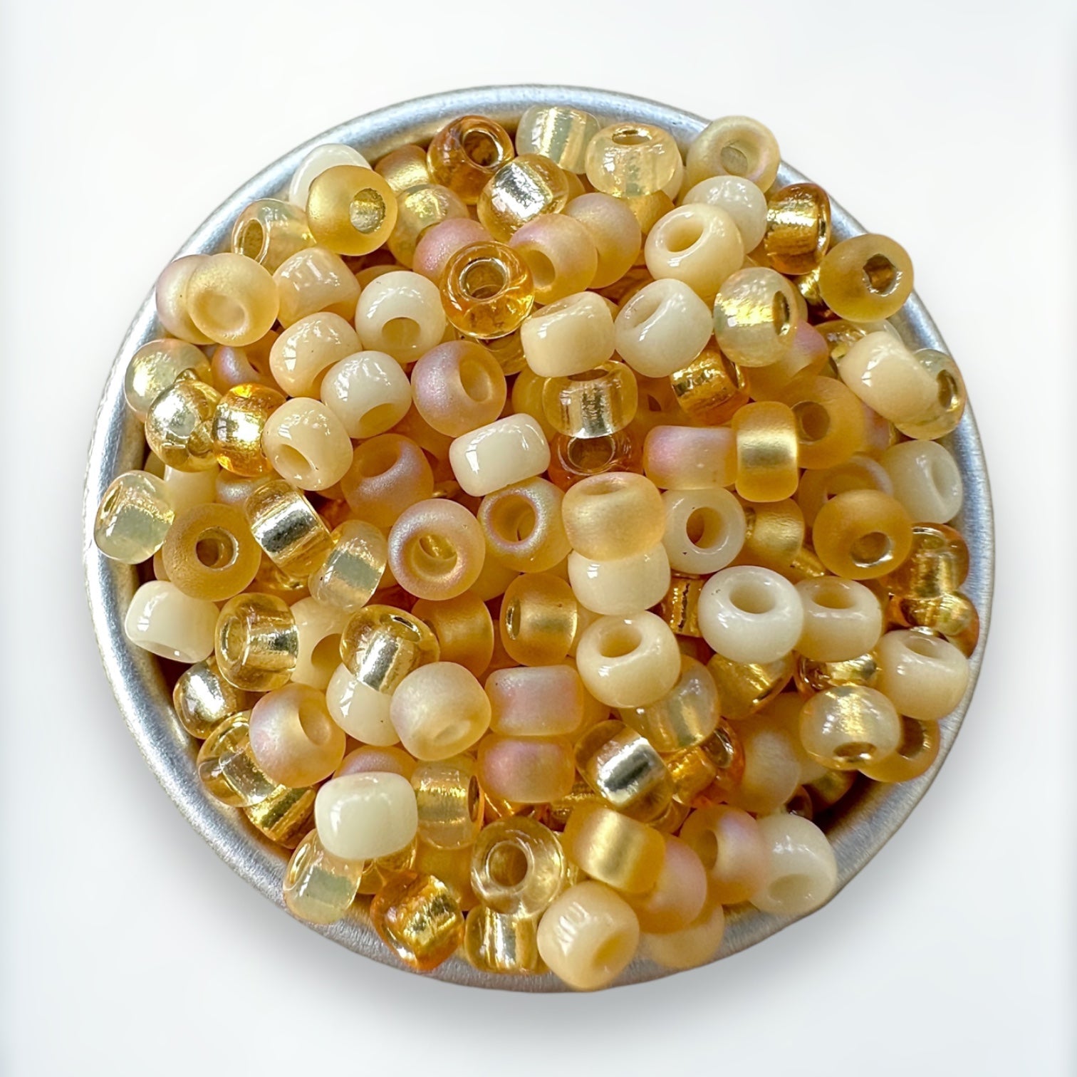 zoomed view of a mix of cream, topaz and gold Miyuki 11/0 seed beads created by The Bead Mix in a round silver tray with a white background
