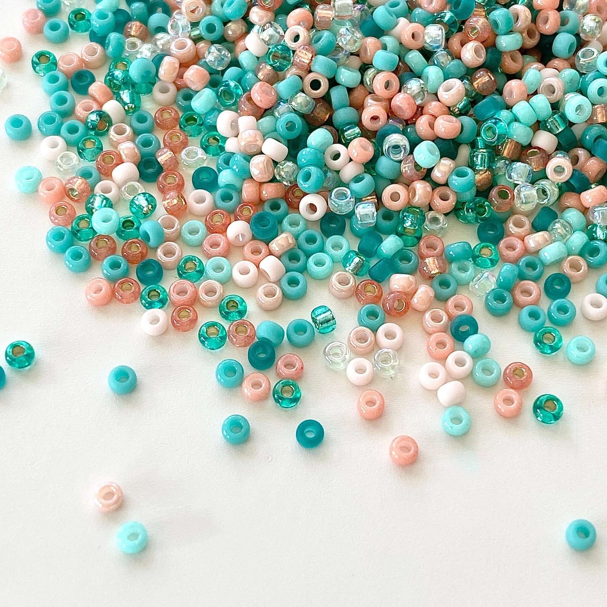 A mix of teal and coral 11/0 Miyuki seed beads spilled onto a white surface