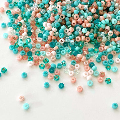 A mix of teal and coral 11/0 Miyuki seed beads spilled onto a white surface