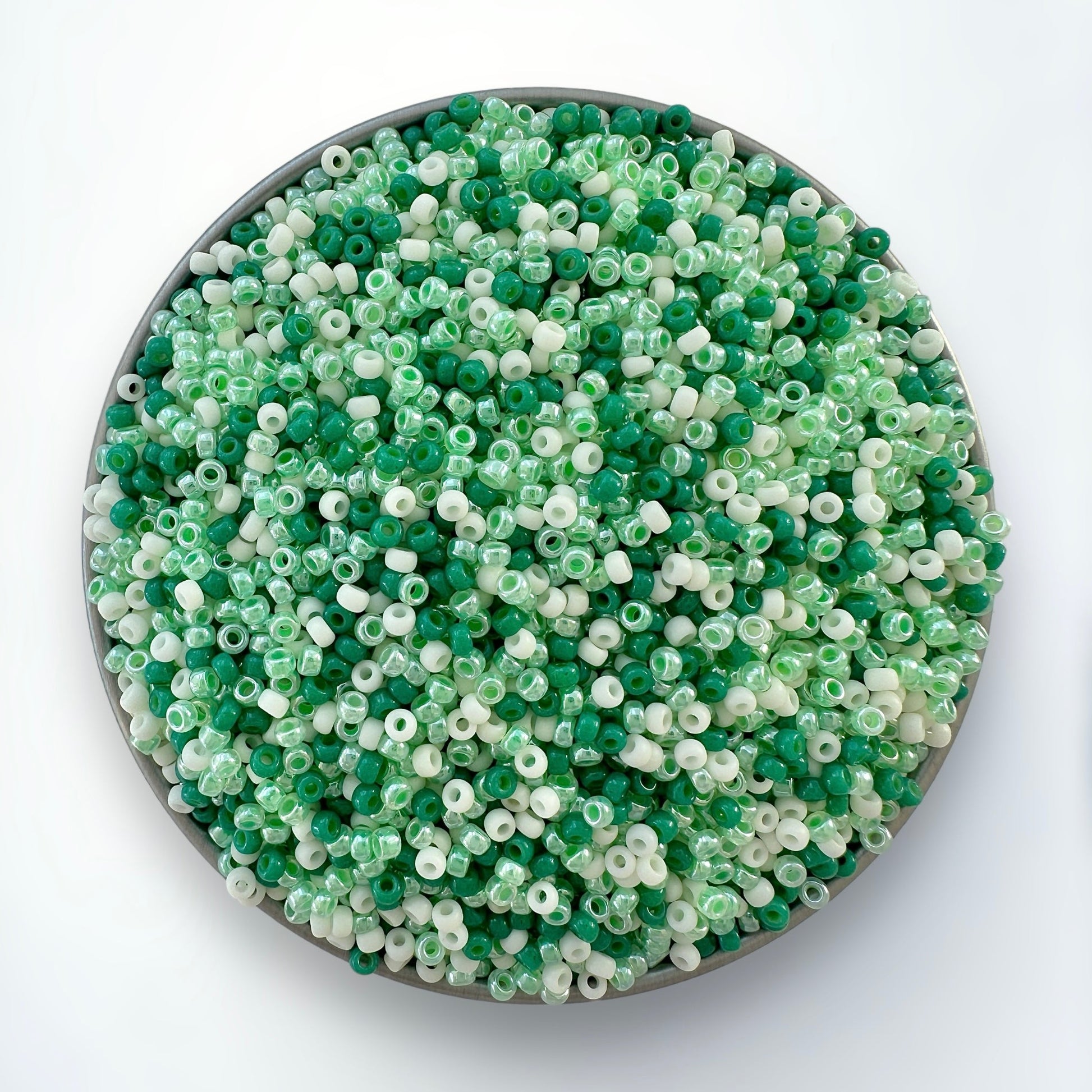 A mix of green and cream Miyuki 11/0 seed beads created by The Bead Mix in a silver container with a white background