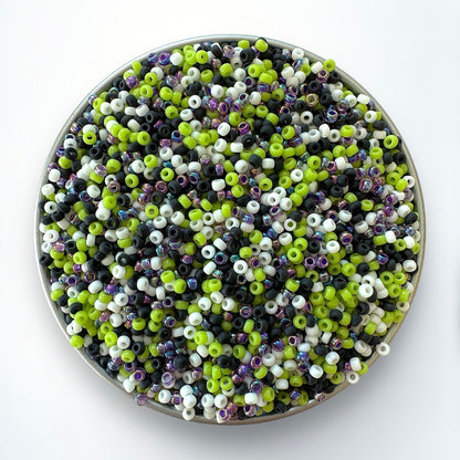 Mix of purple, black, white, and green Miyuki 11/0 seed beads by The Bead Mix in a silver container with a white background